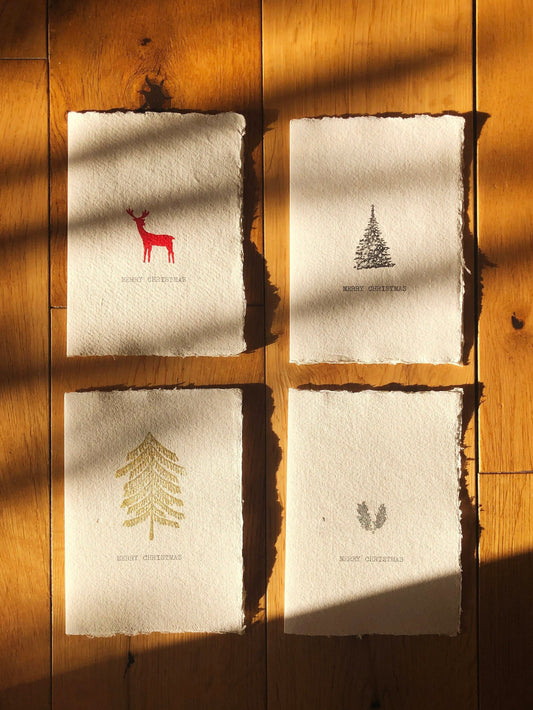 Image of 4 christmas cards on natural handmade paper. Image shows 4 stamp variations, red reindeer, black christmas tree, gold tree and silver holly.